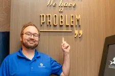 Thumbnail for Man in blue shirt pointing to wall text saying Houston we have a problem in gold letters.