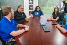 Thumbnail for Five professionals engaged in a meeting around a wooden conference table in a modern office with natural light.