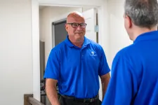 Thumbnail for Two men in blue Brinks polo shirts engaged in conversation inside a bright room with white walls.