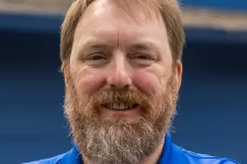 Thumbnail for Smiling man with a beard wearing a blue Braintree polo shirt stands with arms crossed against a blue background.