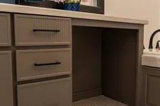 Thumbnail for Brown bathroom vanity with black handles, pink flowers in blue vase, blue towels, and terrazzo floor.