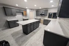 Thumbnail for Modern kitchen with gray cabinets, white countertops, central island, and stainless steel microwave under bright lighting.