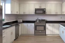 Thumbnail for Modern kitchen with light wood cabinets, black countertops, stainless steel appliances, and hardwood floors