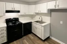 Thumbnail for Modern kitchen with white cabinets, black appliances, stainless steel sink, and wood flooring under ceiling light.