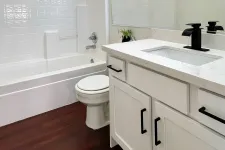 Thumbnail for Modern bathroom with white bathtub, toilet, vanity with black fixtures, and dark wood flooring.