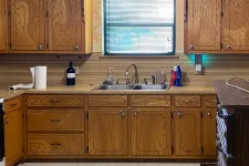 Thumbnail for Vintage kitchen with oak cabinets, double sink below window, countertop accessories, and stove on the side.