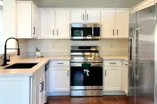 Thumbnail for Modern kitchen with white cabinets, stainless steel appliances, dark wood floor, and black faucet on sink.