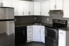 Thumbnail for Modern kitchen corner with white cabinets, stainless steel fridge and oven, black dishwasher, and gray subway tile backsplash.