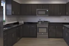 Thumbnail for Modern kitchen with dark wood cabinets, stainless steel appliances, black countertops, and light hardwood flooring