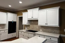 Thumbnail for Modern kitchen with white cabinets, beige tiled backsplash, black stove, and glossy quartz countertops under recessed lighting
