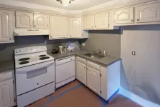Thumbnail for Compact kitchen with white cabinets, electric stove, dishwasher, and single sink, featuring gray countertops and walls.