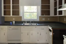 Thumbnail for Empty kitchen with white cabinets, black countertops, dishwasher, and window above double sink under daylight.
