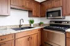 Thumbnail for Modern kitchen with wooden cabinets, granite countertops, stainless steel stove, microwave, and dual sink with plants.