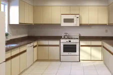 Thumbnail for Modern U-shaped kitchen with cream cabinets, brown countertops, white appliances, and tiled floor under natural light.