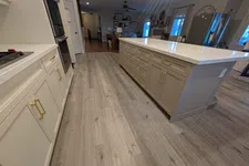 Thumbnail for Modern kitchen with beige cabinets, large white island, gold handles, and light gray wood flooring under warm lighting.