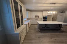 Thumbnail for Modern kitchen with white cabinets, large island, wooden floors, and overhead pendant lighting.