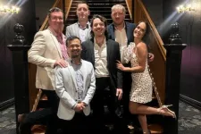 Thumbnail for Group of six people dressed formally posing by a grand staircase in an elegant indoor setting.