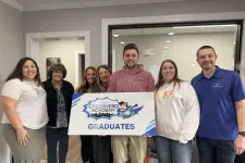Thumbnail for Group of seven people smiling and holding a sign that reads Cyberhero Academy Graduates inside an office.