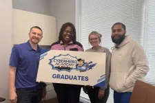 Thumbnail for Four diverse graduates smiling and holding a ComTec CyberHero Academy Graduates sign in an office setting.
