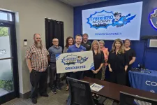 Thumbnail for Group of diverse graduates holding CyberHero Academy sign in office celebrating completion.