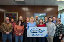 Thumbnail for Group of diverse graduates holding a Cyberhero Academy sign in an office setting with wooden walls and framed art.