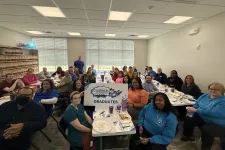 Thumbnail for Group of Cyberhero Academy graduates seated around tables in a bright room holding a graduates sign.