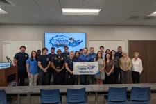Thumbnail for Group of graduates and instructors posing with CyberHero Academy banner in a classroom setting with a police emblem.