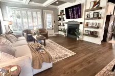 Thumbnail for Cozy living room with beige sofa, armchairs, wooden flooring, fireplace, mounted TV, and decorative shelves.