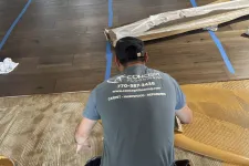Thumbnail for Flooring installer in Concept Flooring shirt spreading adhesive on floor preparing for hardwood installation.