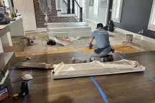 Thumbnail for Worker installing hardwood flooring in a living room undergoing renovation with tools and materials scattered around.