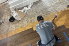 Thumbnail for Worker installing dark wood laminate flooring over underlayment with tools in a room under renovation.