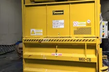 Thumbnail for Large yellow industrial baler machine labeled M60-CB in a warehouse with caution signs and instructions.