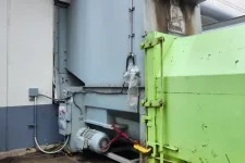 Thumbnail for Industrial waste compactor with green container in a facility's outdoor area near concrete ground.