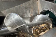 Thumbnail for Close-up of a large industrial metal screw conveyor inside a container with wood chips.