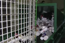 Thumbnail for Disposable cups entering a green recycling machine conveyor belt behind a metal safety grid