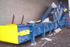 Thumbnail for Industrial blue and yellow conveyor belt system inside warehouse with scattered debris on floor.