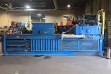 Thumbnail for Large blue industrial baler machine inside a warehouse with concrete floor and metal shelves nearby.