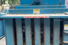 Thumbnail for Rusty blue industrial trash compactor with caution signs and visible compressed waste inside.