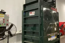 Thumbnail for Large green industrial baler machine inside warehouse with control panel and standing fan nearby