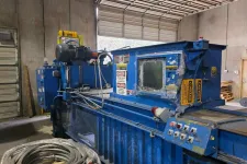 Thumbnail for Blue industrial machine with control panel inside a warehouse near coiled cables and open garage door.