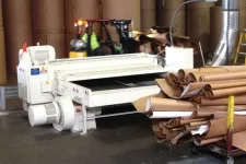 Thumbnail for Industrial paper manufacturing equipment with large rolls of brown paper and forklift in warehouse.