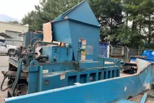 Thumbnail for Large blue industrial machine with hydraulic components and chute in outdoor fenced area near trees and vehicles.
