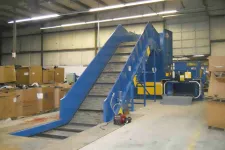 Thumbnail for Blue industrial conveyor belt system in warehouse surrounded by cardboard boxes and equipment