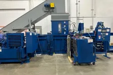 Thumbnail for Large blue industrial baler machine with conveyor belt in a factory setting on concrete floor.