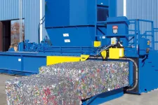 Thumbnail for Industrial blue recycling baler compresses crushed aluminum cans into large compact bales outdoors.