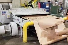 Thumbnail for Industrial machine processing large rolls of brown kraft paper in a factory setting with yellow safety railings.