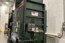 Thumbnail for Large green industrial machine with control panel and cables in a warehouse with concrete floor and high ceiling.