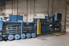 Thumbnail for Large industrial baler machine with multiple rollers inside a warehouse with concrete walls and garage doors.