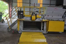 Thumbnail for Industrial yellow waste compactor machine inside a warehouse with safety railings and control panel.