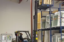 Thumbnail for Man operating yellow Yale forklift lifting wooden panels in a spacious warehouse with organized shelves.